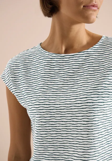 Halbkörperansicht einer Frau in schlichtem weißem T-Shirt mit feinen, schwarzen Wellenstreifen.