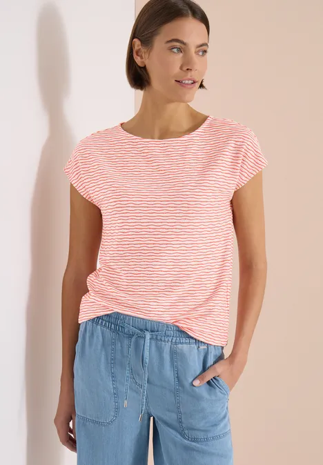 Frau trägt gestreiftes rosa-weißes T-Shirt und hellblaue lockere Jeanshose vor hellem Hintergrund.