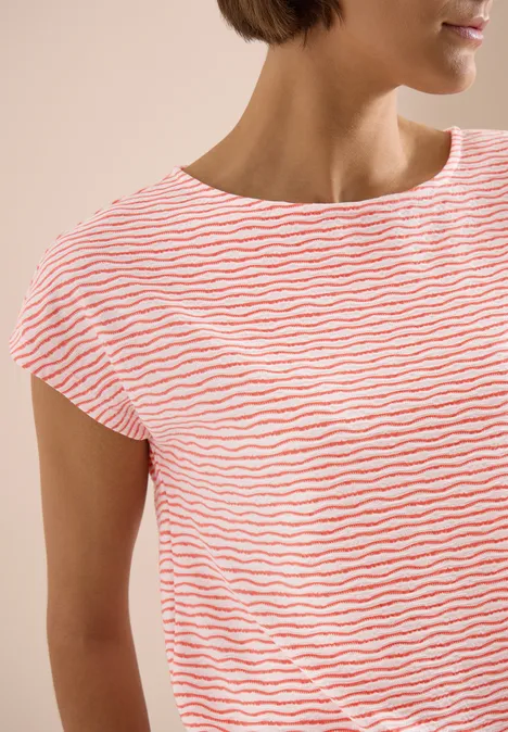 Frau in weißem T-Shirt mit orange Streifen, kurzen Ärmeln und rundem Halsausschnitt vor beigem Hintergrund