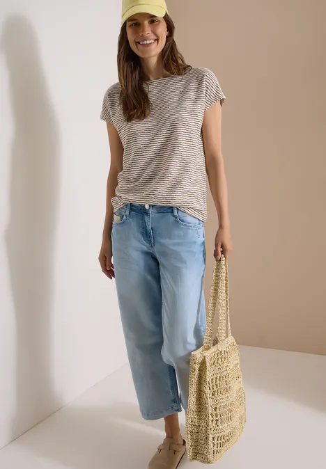 Femme en t-shirt rayé, jean ample et sac en paille tressée.