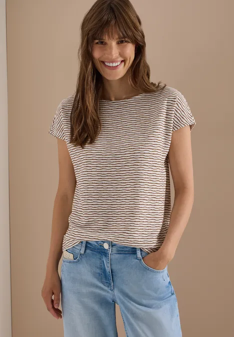 Femme en t-shirt rayé et jean bleu clair, style décontracté, devant un mur beige