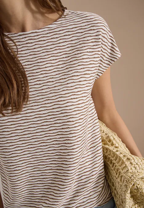 Personne portant un t-shirt blanc à rayures brunes et tenant un sac en paille tressée.