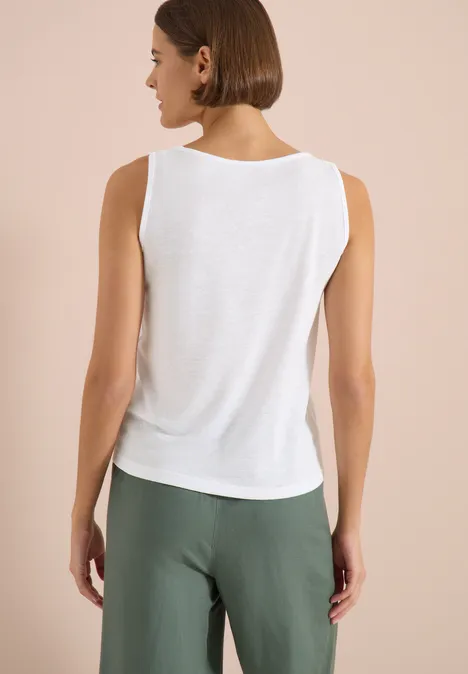 Top avec col en V arrondi et détail tressé White Femme de dos portant un débardeur blanc et un pantalon vert sur fond clair.