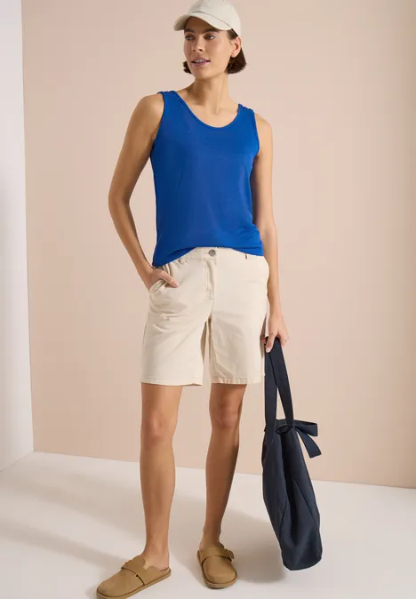 Top avec col en V arrondi et détail tressé surf blue Personne porte un débardeur bleu, un short beige et tient un sac bleu marine.