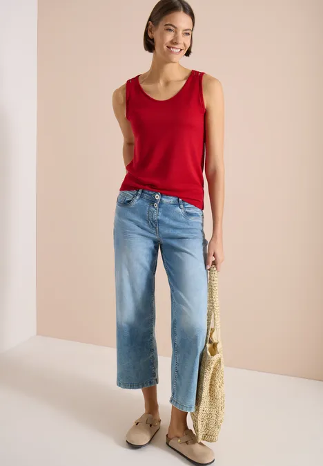 Top avec col en V arrondi et détail tressé tamarillo red Femme portant un débardeur rouge, jean large court bleu, sac en paille et mocassins beiges devant un fond neutre.