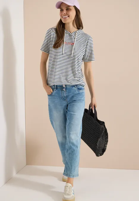 Shirt met korte mouwen, capuchon en glitter vanilla white Vrouw in gestreept shirt, blauwe jeans en gevlochten tas.