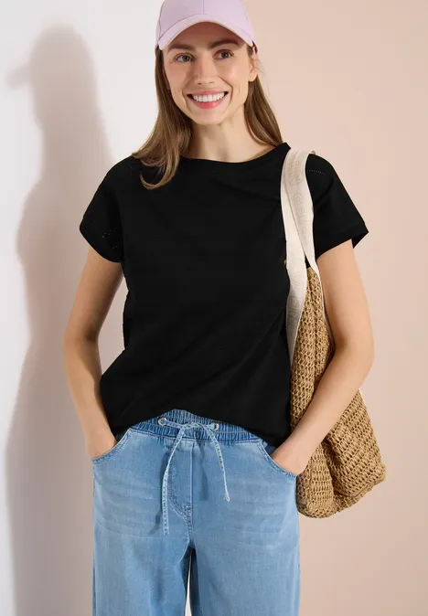 Frau in schwarzem T-Shirt und Jeans mit Stroh-Tasche über der Schulter.