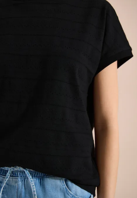 Person trägt schwarzes T-Shirt mit feinen Streifen und blaue Jeans, Oberkörperansicht ohne Gesicht