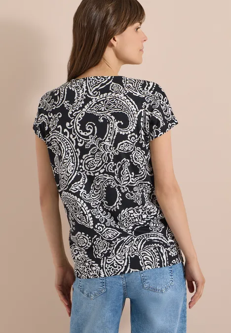 T-Shirt mit V-Neck und Print Black Frau von hinten in blauen Jeans und schwarzem T-Shirt mit weißem Paisley-Muster vor beigem Hintergrund.