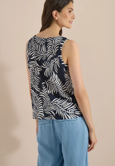 Top met split in de hals en tweekleurig patroon universal blue Vrouw van achteren in mouwloos marineblauw topje met witte bladerenprint en lichtblauwe spijkerbroek.