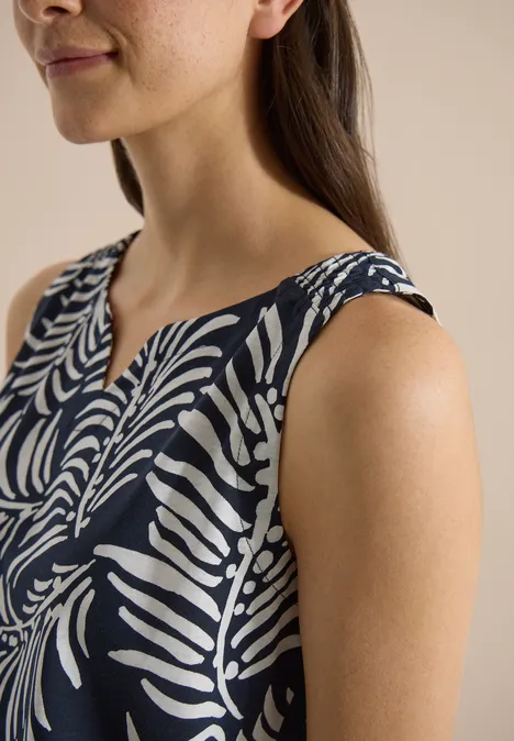 Top met split in de hals en tweekleurig patroon universal blue Een vrouw draagt een mouwloze donkerblauwe top met wit bladmotief.