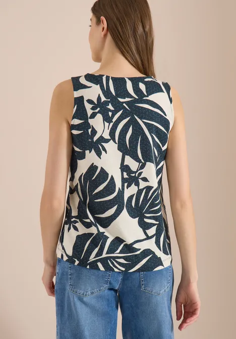 Top met ronde hals en bladprint palm breeze green Achteraanzicht van vrouw in mouwloze top met donkerblauw bladmotief en spijkerbroek.