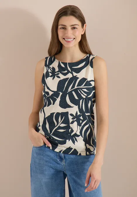 Top met ronde hals en bladprint palm breeze green Vrouw draagt mouwloze top met groot marinebladprint en spijkerbroek.