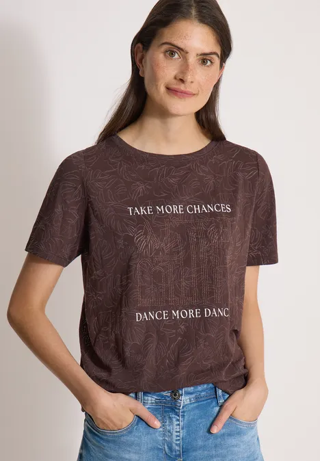 T-Shirt in Ausbrenner-Optik brown cacao Frau trägt braunes T-Shirt mit weißem Schriftzug 'TAKE MORE CHANCES, DANCE MORE DANCE' und Jeans.