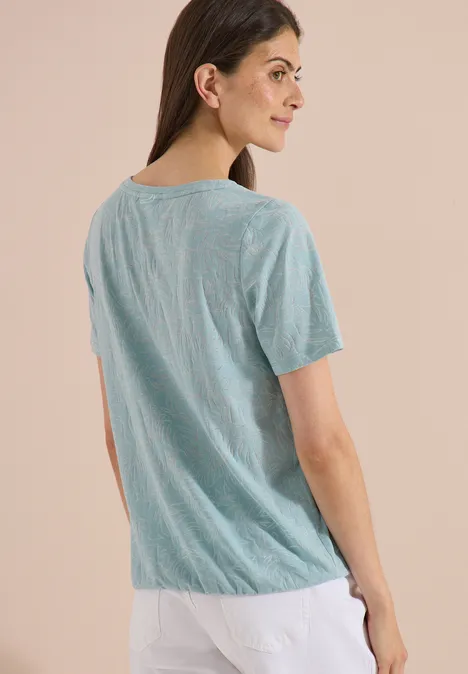 T-Shirt in Ausbrenner-Optik crystal mint Rückansicht einer Person in grünem T-Shirt und weißer Hose vor neutralem Hintergrund.
