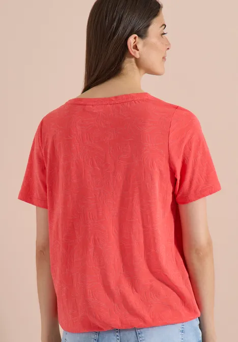 T-Shirt in Ausbrenner-Optik coral Rückansicht einer Person in einem korallefarbenen T-Shirt vor beigem Hintergrund.