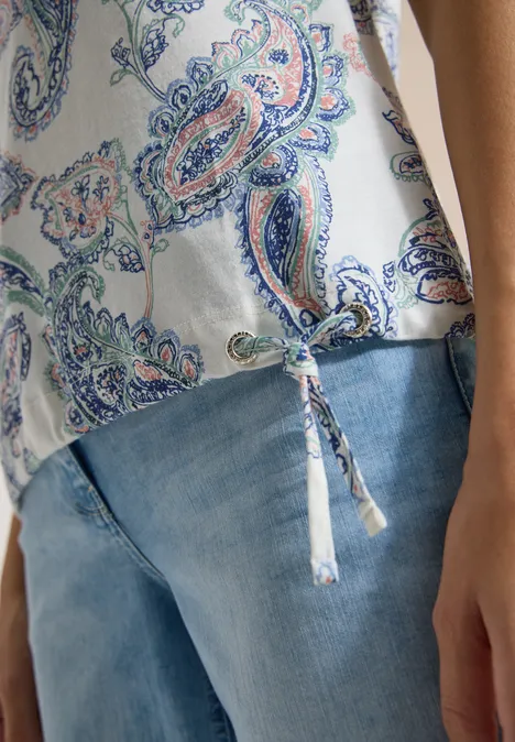 Hemd mit Paisley-Muster und dekorativem Knoten über hellen Jeans.