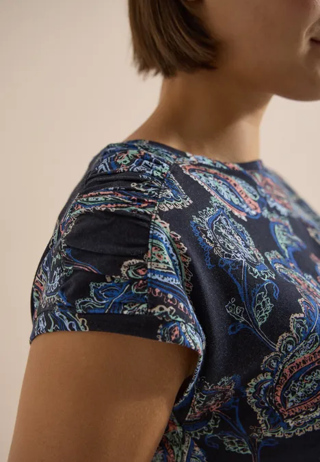 Een persoon draagt een donkerblauw T-shirt met korte mouwen en een bont paisley-patroon.