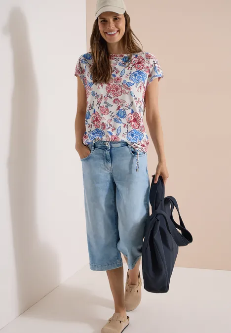 Kurzarm Shirt mit Boatneck und Raffung vanilla white Frau trägt geblümtes T-Shirt, weite Jeans und hält eine blaue Tasche.