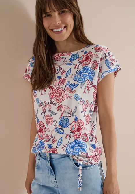 Kurzarm Shirt mit Boatneck und Raffung vanilla white Frau im weißen Shirt mit blau-rotem Blumenprint und Jeans vor hellem Hintergrund.
