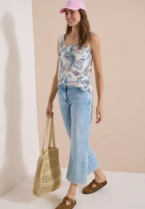 Top mit gerundetem V-Neck und Flechtdetail vanilla white Model trägt helle Jeans und gemustertes Top, dazu Strohtasche und braune Sandalen.