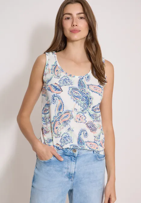 Top mit gerundetem V-Neck und Flechtdetail vanilla white Frau trägt weißes Tanktop mit pastellfarbenem Paisley-Muster und hellblauer Jeans, Hände in den Taschen.