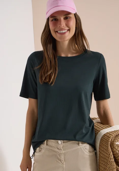 Frau mit dunkelgrünem T-Shirt, beiger Hose und Korbtasche