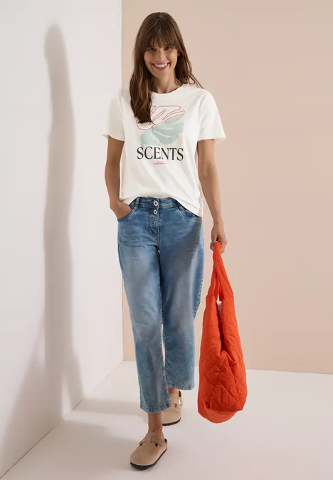 T-Shirt mit Rundhals und Frontprint vanilla white Eine Frau trägt weißes T-Shirt mit Schriftzug, weite Jeans, bequeme Schuhe und hält eine orange Jacke.