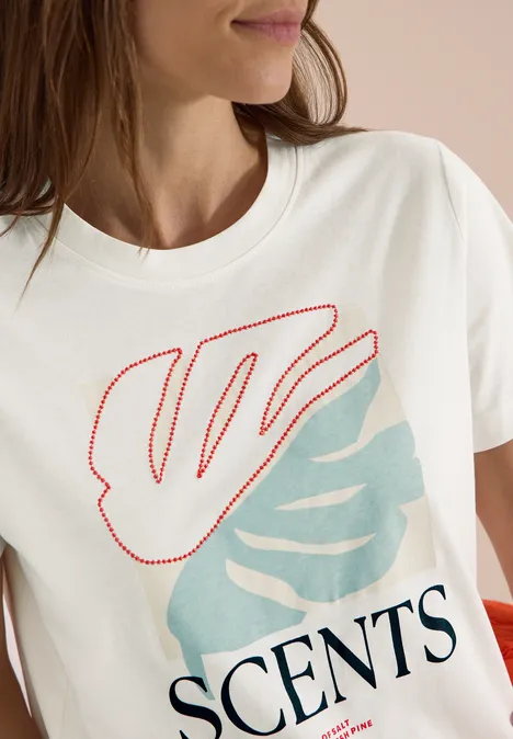 T-Shirt mit Rundhals und Frontprint vanilla white Eine Frau trägt ein weißes T-Shirt mit roten und hellblauen Blattmotiven und dem Schriftzug 'SCENTS'.