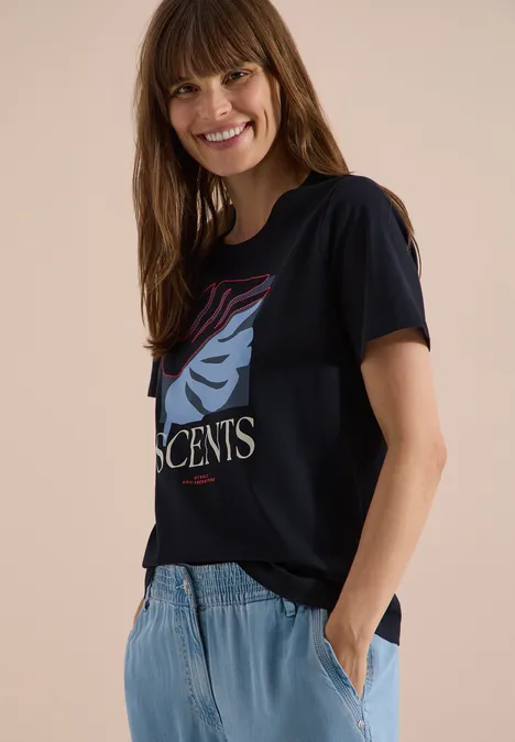 T-Shirt mit Rundhals und Frontprint universal blue Frau trägt schwarzes T-Shirt mit stilisiertem Gesicht, hellblaue Jeans, steht seitlich mit Hand in Tasche.
