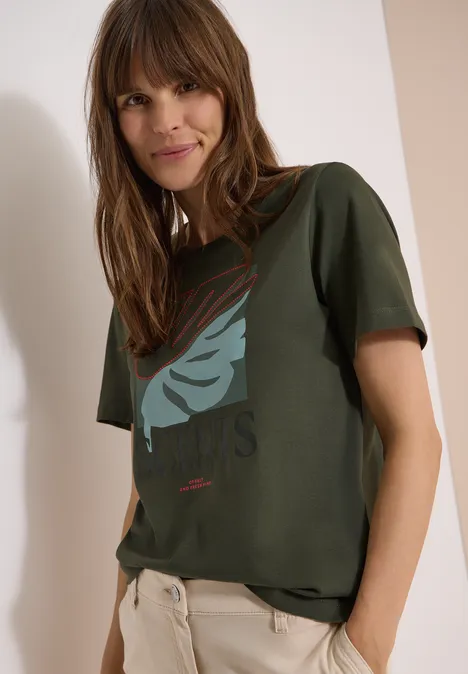 T-Shirt mit Rundhals und Frontprint khaki Eine Person trägt ein grünes T-Shirt mit Vogelmotiv und eine helle Hose vor neutralem Hintergrund.
