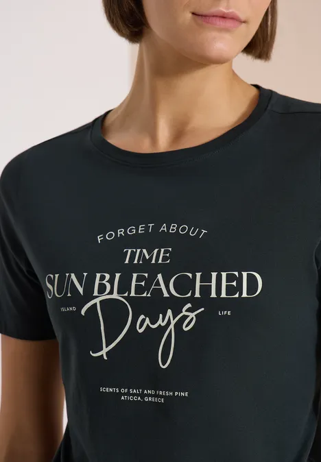 T-Shirt mit Boat Neck und Wording Artwork palm breeze green Frau in schwarzem T-Shirt mit weißem Schriftzug 'Forget about time sun bleached days'.