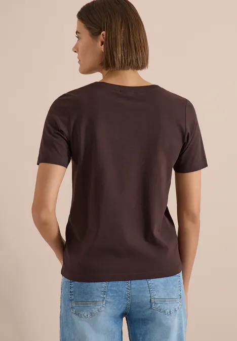 T-Shirt mit Boat Neck und Wording Artwork brown cacao Eine von hinten gesehene Person trägt ein braunes T-Shirt und blaue Jeans vor beigem Hintergrund.