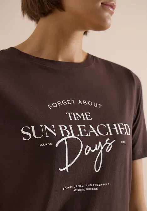 T-Shirt mit Boat Neck und Wording Artwork brown cacao Braunes T-Shirt mit weißem Slogan 'Forget About Time. Sun Bleached Days.' getragen von einer Frau.