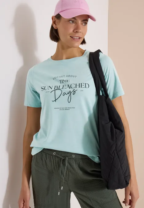 T-Shirt mit Boat Neck und Wording Artwork crystal mint Frau trägt mintfarbenes T-Shirt mit Aufschrift „Sun Bleached Days“ und schwarze Schultertasche.