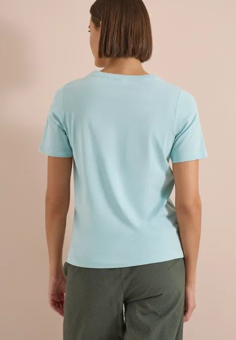 T-Shirt mit Boat Neck und Wording Artwork crystal mint Frau mit kurz geschnittenem Haar trägt ein hellblaues T-Shirt und dunkelgrüne Hose, Ansicht von hinten.