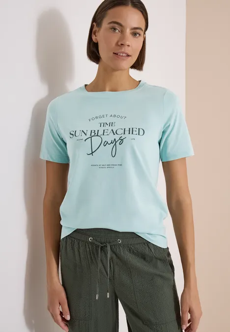 T-Shirt mit Boat Neck und Wording Artwork crystal mint Frau trägt hellblaues T-Shirt mit Aufdruck 'SUN BLEACHED Days' und dunkelgrüne Hose.