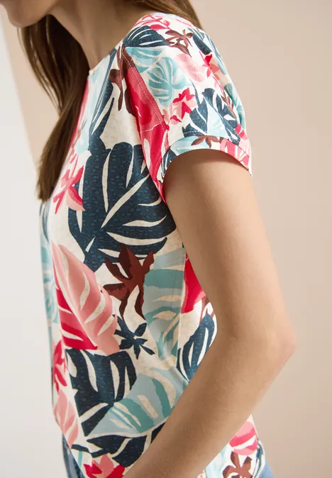 Zijaanzicht van een persoon in een kleurrijk t-shirt met tropische print tegen een lichte achtergrond.