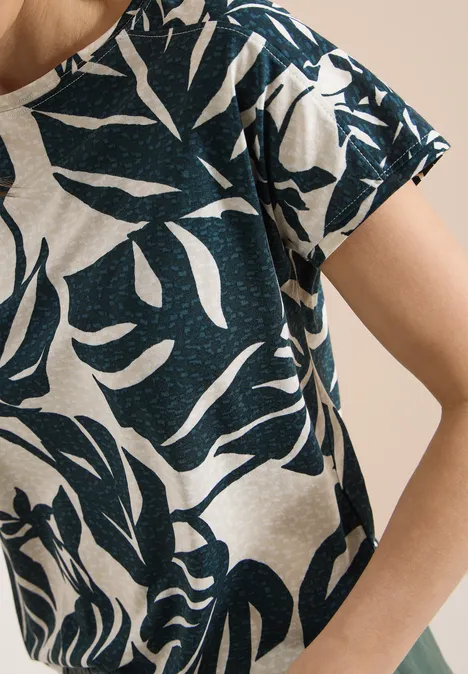 Close-up van een beige T-shirt met donkerblauw, abstract bladpatroon op schouder en arm.