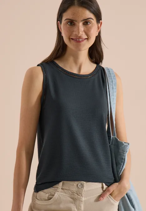 Top met boothals en kanten details palm breeze green Frau mit dunkelblauem ärmellosem Oberteil und Tasche über der Schulter.