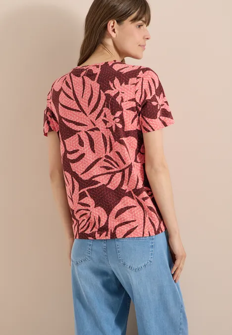 T-Shirt mit Rundhals und Blätterprint coral Frau von hinten in rosa T-Shirt mit schwarzem Blattmuster und lockeren blauen Jeans.