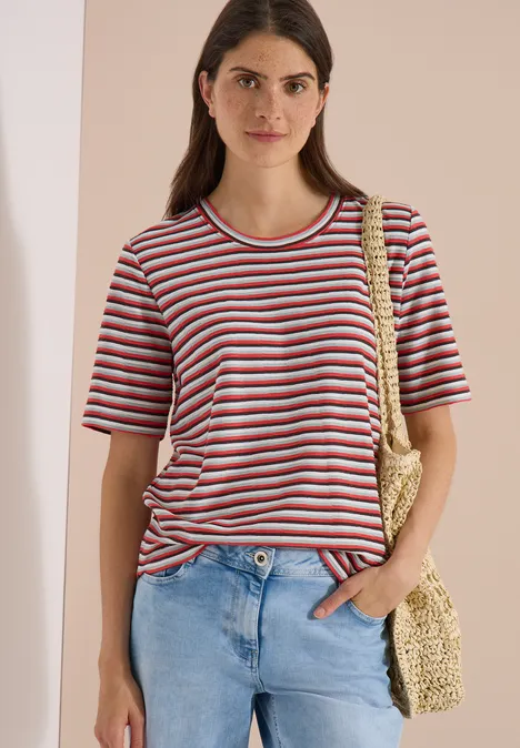 T-Shirt mit Struktur und Streifen brown cacao Frau in gestreiftem T-Shirt, Jeans und Strohtasche vor beigem Hintergrund.