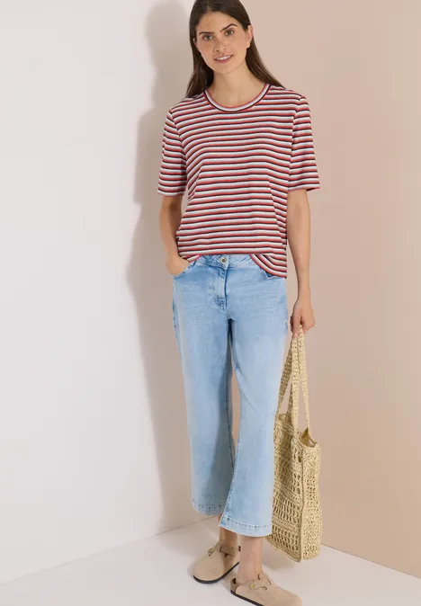 T-Shirt mit Struktur und Streifen brown cacao Frau trägt gestreiftes T-Shirt, helle Jeans und hält eine geflochtene Strohtasche, steht vor heller Wand.