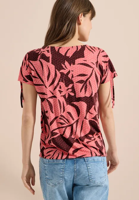 Vrouw van achteren in een roze bladprintshirt en een blauwe spijkerbroek.