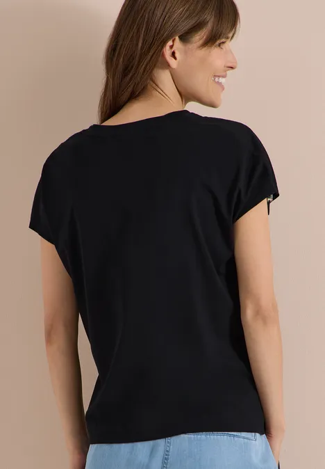 T-Shirt mit Raffung in Unifarbe Black Frau von hinten in schwarzem T-Shirt und blauer Jeans vor beigem Hintergrund.