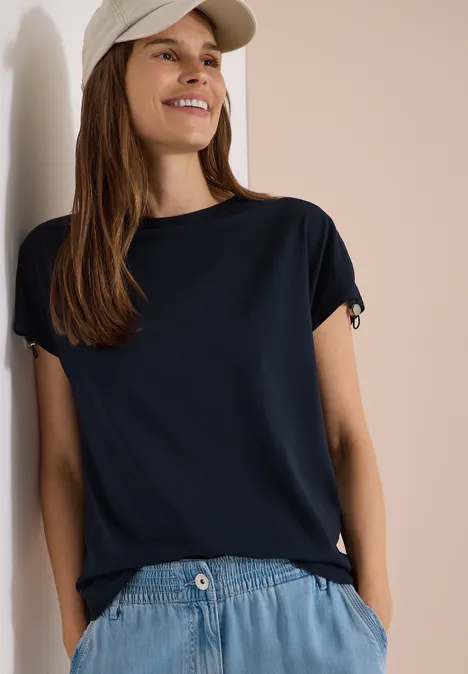 T-Shirt mit Raffung in Unifarbe universal blue Eine Person trägt ein dunkelblaues T-Shirt, helle Jeans und eine helle Cap, lehnt an einer hellen Wand.