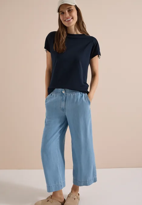 T-Shirt mit Raffung in Unifarbe universal blue Frau in dunkelblauem T-Shirt, hellblauer Culotte-Hose und Sandalen vor neutralem Hintergrund.