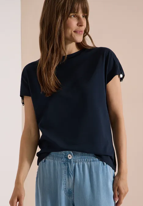 T-Shirt mit Raffung in Unifarbe universal blue Frau in dunkelblauem T-Shirt und hellblauem Jeansrock vor beigem Hintergrund.