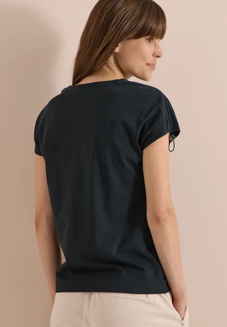 T-Shirt mit Raffung in Unifarbe palm breeze green Frau von hinten in schlichtem schwarzem Shirt, Hände lässig in den Taschen