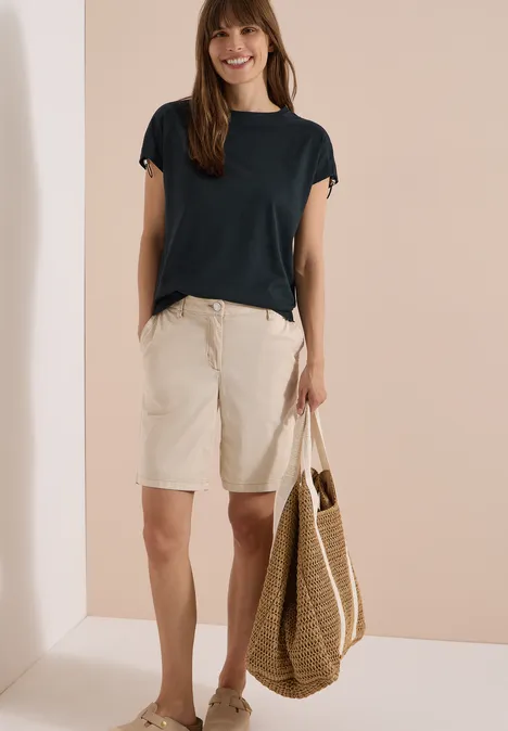 T-Shirt mit Raffung in Unifarbe palm breeze green Frau trägt dunkelblaues T-Shirt, beige Bermuda-Shorts und eine Strohtasche.